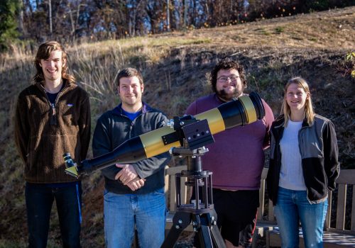 four people standing with a telescope